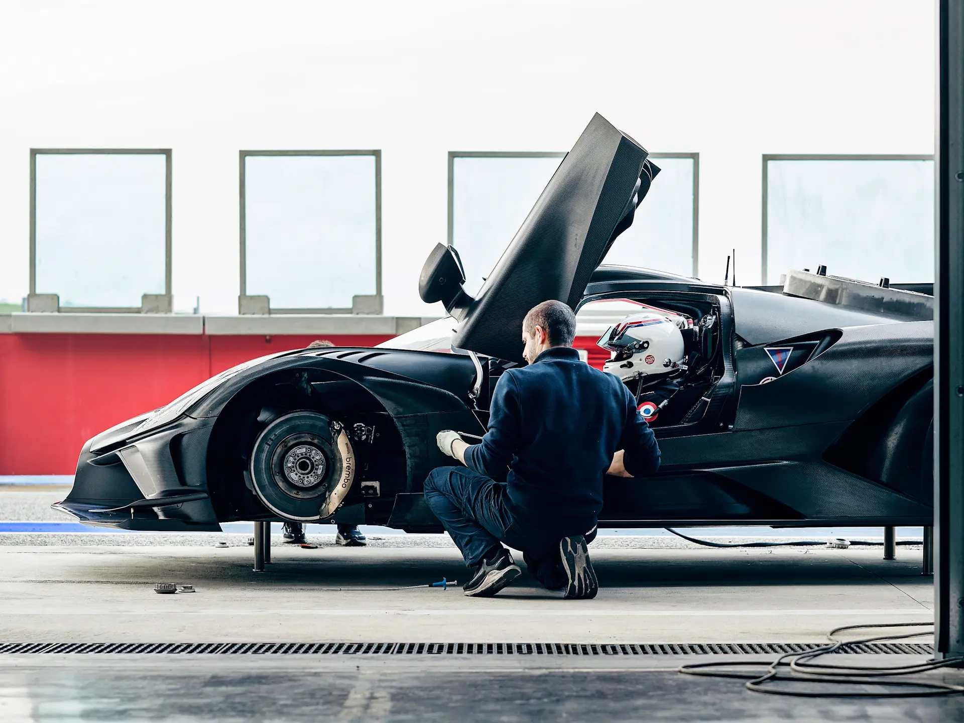 Mechanics work on a wheel-less Bolide in pits, exposing the brembo carbon brakes